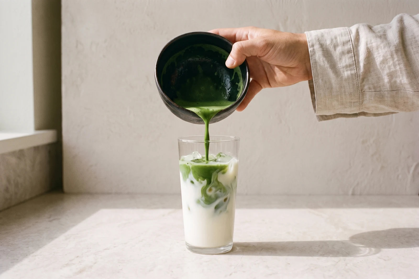 Aufgeschlagener Matcha, aus der Teeschale auf kalte Milch und Eis gegossen